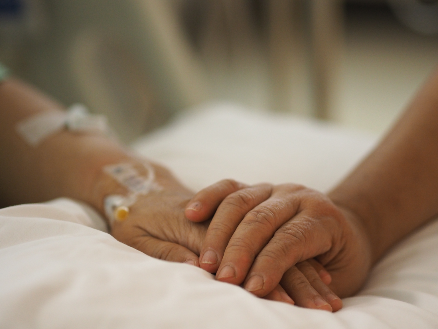 Woman holding an elderly woman's hand. The elderly woman has an IV.